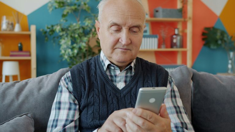 Older man using a smartphone on the couch at home